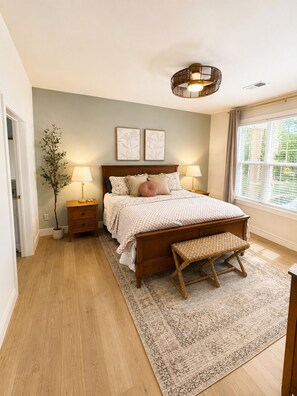Ein Schlafzimmer mit einem hölzernen Bett, zwei Nachttischen, einer Bank, einer Stehlampe und einer Wandleuchte.