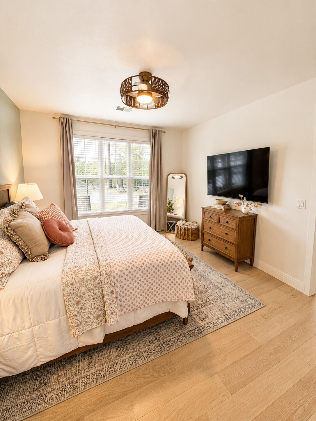 A bedroom with a bed, a dresser, a television, and a window with curtains.
