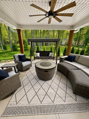 Eine Terrasse im Freien mit Korbmöbeln, einer Schaukel und einem Deckenventilator.