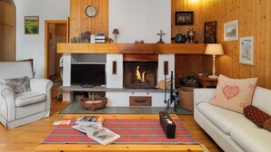 Een gezellige woonkamer met een open haard, een bank, een salontafel met tijdschriften en een televisie.