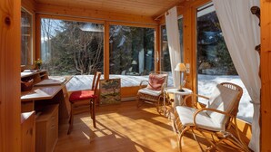 Een gezellig houten interieur met houten wanden en vloeren, grote ramen, een eethoek en een zithoek met rieten stoelen.