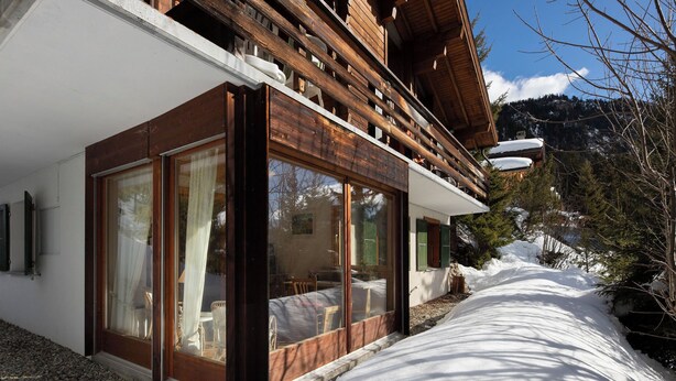 Een modern chalet met grote glasramen, een houten gevel en een sneeuwbedekte pad naar de ingang.