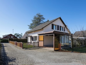 Ein modernes Haus mit überdachter Terrasse, eingezäuntem Garten und Kopfsteinpflasterauffahrt.