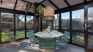 A sunlit patio with a round table set for dining, surrounded by striped chairs, and a hanging plant above.