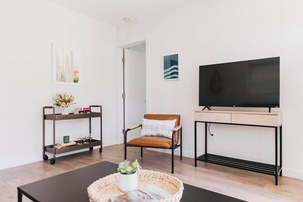 Ein modernes Wohnzimmer mit einem Flachbildfernseher, einem braunen Ledersessel, einem kleinen Tisch mit einer Pflanze und einem Metallwagen mit Büchern und einer Vase.