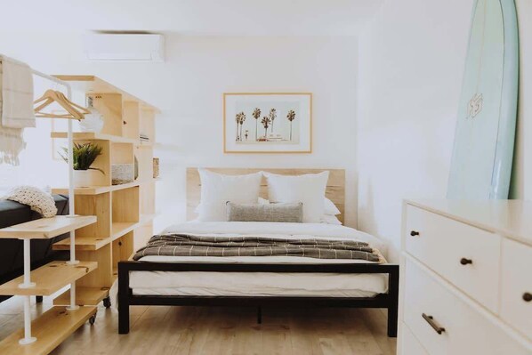 A bedroom with a bed, a wooden shelf unit, a dresser, and a framed picture on the wall. - Spacious, Designed Ocean Loft in Solana Beach! (Solana Beach)