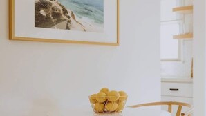 A dining area with a round table, two wooden chairs, a framed picture on the wall, and a basket of lemons on the table. - Spacious, Designed Ocean Loft in Solana Beach! (Solana Beach)