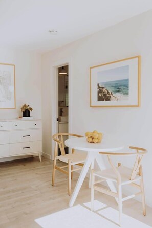 A modern, minimalist room with a white dresser, a round table with chairs, and framed pictures on the walls.