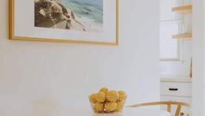 Una habitación minimalista con una mesa redonda blanca, dos sillas de mimbre y un cuadro con una playa.