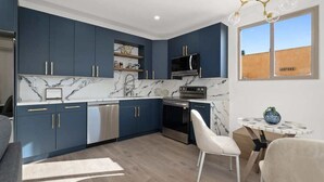A modern kitchen with dark blue cabinets, a marble backsplash, and a built-in oven. There is a dining area with a white table and chairs. - Refined Retreat in Banker's Hill (San Diego)