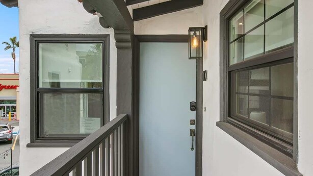 Ein Gebäudeeingang mit Glastür, einem kleinen Balkon mit Geländer und einem Fenster mit Leuchte.