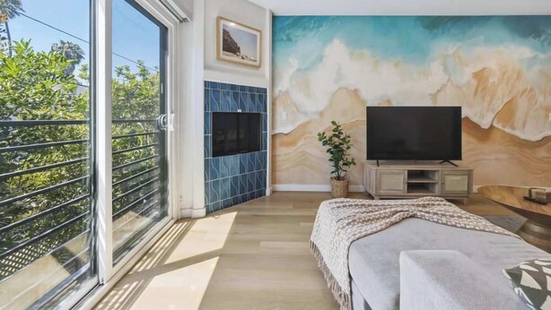Een slaapkamer met een televisie, een muurschildering, een balkon en uitzicht op groen.