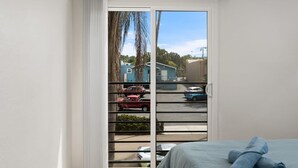Een slaapkamer met een bed en een raam met uitzicht op geparkeerde auto's en huizen.