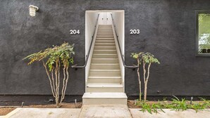 Een trap die leidt naar appartementenummers 204 en 203, met een donkere muur en kleine planten aan de voet.