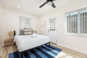 Un dormitorio con cama, ventilador de techo, puerta y ventanas con persianas.