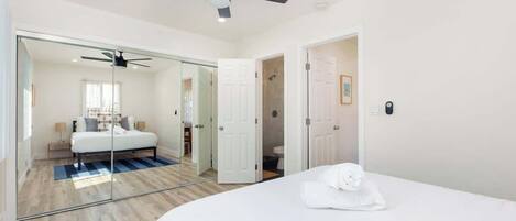 A modern hotel room with a large bed, a ceiling fan, and a glass partition separating the bedroom from the bathroom.