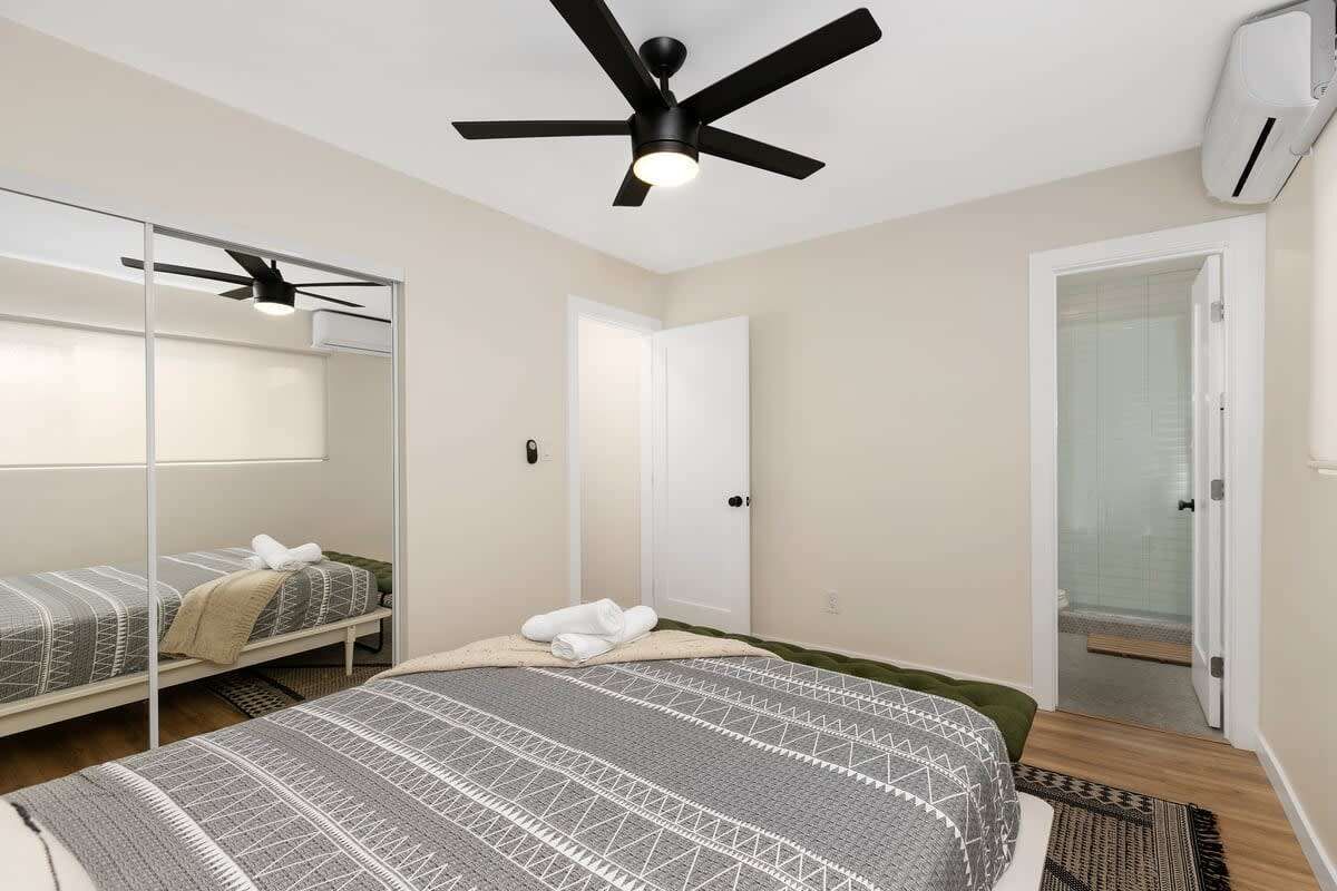 A bedroom with a bed, a ceiling fan, a wardrobe, and a door leading to a bathroom.