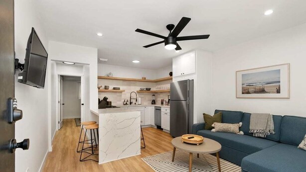 Una sala de estar moderna con un sofá azul, una mesita redonda y una zona de cocina con un refrigerador y un televisor.