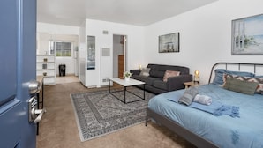 A bedroom with a bed, a sofa, a coffee table, and a painting on the wall. - Steps Away from PB Beaches + Hot Tub (San Diego)
