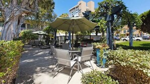 An outdoor seating area with tables and chairs, surrounded by greenery and trees. - Steps Away from PB Beaches + Hot Tub (San Diego)