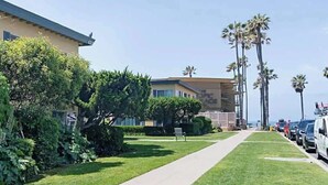 A residential street with a row of parked cars, a sidewalk, and tall palm trees. - Steps Away from PB Beaches + Hot Tub (San Diego)