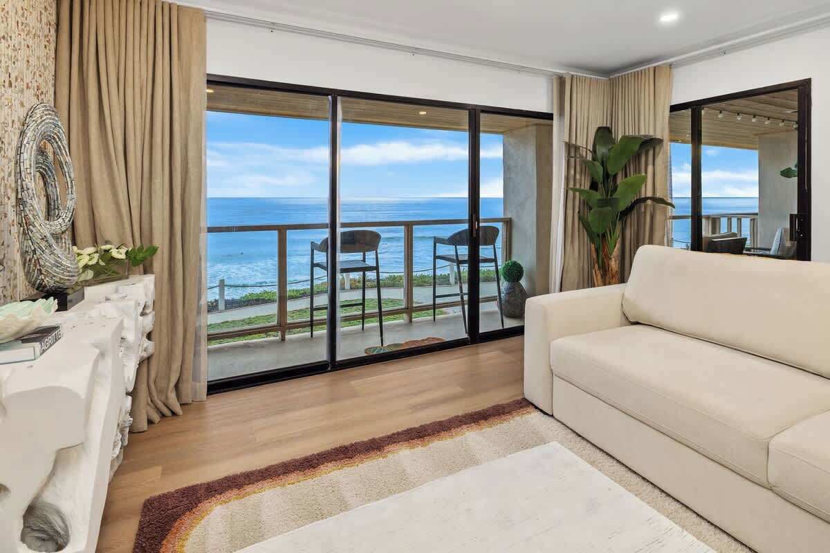 Ampla sala de estar com uma grande porta de vidro deslizante que dá para uma varanda com vista para o oceano.