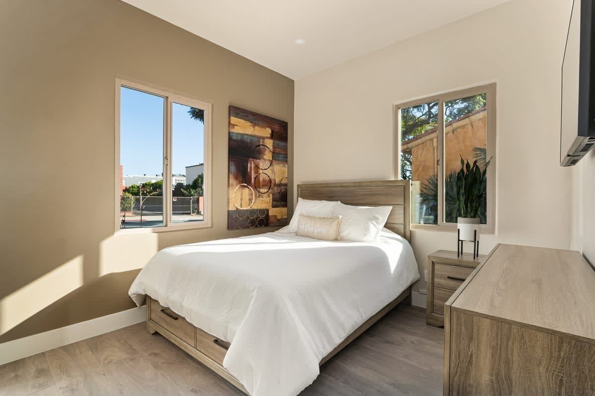 A bedroom with a large bed, a wooden nightstand, a desk, and a window with a view of the outside.