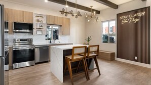 Une cuisine moderne dotée d’un îlot central, d’appareils électroménagers en acier inoxydable et d’un luminaire suspendu.