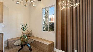 Un intérieur moderne avec un banc en bois, une table à plateau en verre sur laquelle est posée une plante en pot, un luminaire au plafond et un mur avec des lambris en bois verticaux, ainsi que le texte « RESTEZ CHICS, San Diego ».