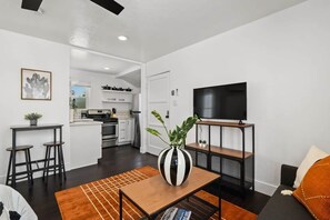 A modern living room with a TV, a dining area with stools, and a kitchen visible through an open door. - Perfect Studio in the Best Location of North Park! (San Diego)