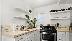 A modern kitchen with white cabinets, stainless steel appliances, and a window with blinds. - Perfect Studio in the Best Location of North Park! (San Diego)