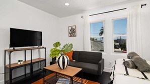 A modern living room with a flat-screen TV, a sofa, a coffee table with a plant, and a bed with a rolled towel. - Perfect Studio in the Best Location of North Park! (San Diego)