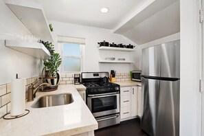 A modern kitchen with white cabinets, stainless steel appliances, and a window providing natural light. - Perfect Studio in the Best Location of North Park! (San Diego)