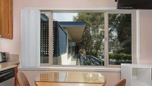 A kitchen with a dining table and chairs, a window with a view of a building and trees, and a white cabinet. - PB Local Living Beach Access Less Than a Block (San Diego)