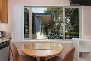 Una cucina con tavolo e sedie, una finestra vista su un edificio e alberi, e un armadietto bianco.