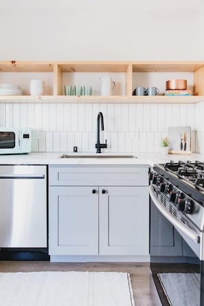 Een moderne keuken met witte kasten, een roestvrijstalen vaatwasser, een zwarte kraan en een gasfornuis.