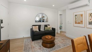 A modern living room with a dark sofa, a round coffee table, and a large mirror on the wall. - Modern Spanish Living in Prime Location Area (San Diego)