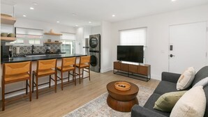 A modern kitchen with a central island, bar stools, a large TV, and a sofa in a living area. - Modern Spanish Living in Prime Location Area (San Diego)
