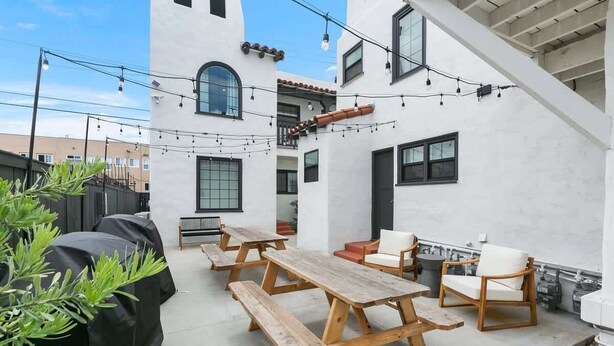 A patio area with wooden picnic tables and chairs, surrounded by white walls and a clear sky. - Modern Spanish Living in Prime Location Area (San Diego)
