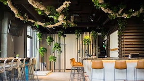 Un espace bar moderne avec un long comptoir, de nombreux tabourets et des plantes suspendues.