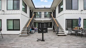 Een modern gebouw met een centrale trap, een overdekt terras en een fiets nabij de ingang.