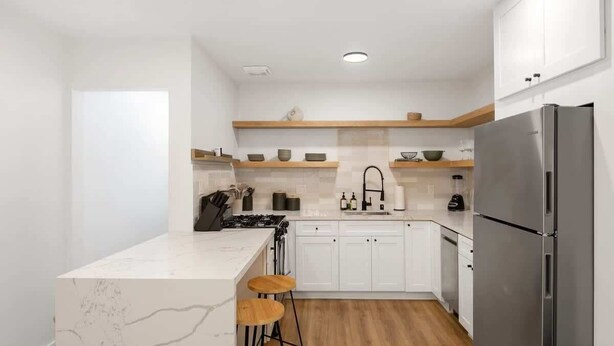 Een moderne keuken met witte kastjes, een marmeren eiland, houten krukken en een roestvrijstalen koelkast.