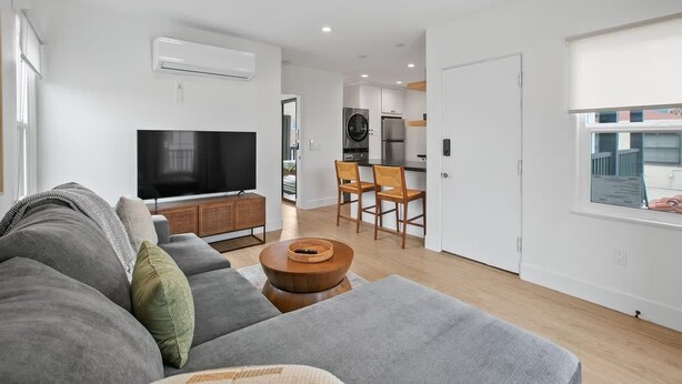 Una sala de estar moderna con un sofá gris, un televisor y una zona de comedor con sillas y una mesa.