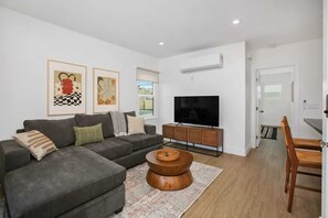 A modern living room with a sectional sofa, a flat-screen TV, and a dining area with a wooden table and chairs.