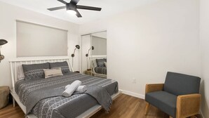 Ein Schlafzimmer mit Bett, Sessel, Deckenventilator und Spiegel.