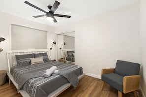 Ein Schlafzimmer mit Bett, Sessel, Deckenventilator und Spiegel.