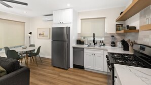 Eine moderne Küche mit weißen Schränken, einem Edelstahl-Kühlschrank, einem Gasherd und einem Essbereich mit Tisch und Stühlen.