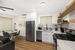 Eine moderne Küche mit weißen Schränken, einem Edelstahl-Kühlschrank, einem Gasherd und einem Essbereich mit Tisch und Stühlen.