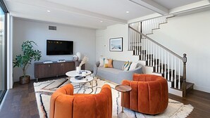 Un salon moderne avec un canapé, des poufs et un téléviseur.