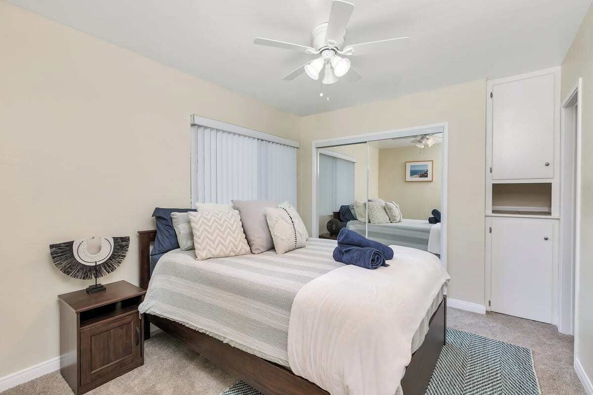 Une chambre à coucher comprenant un lit, une table de chevet, un ventilateur de plafond, un miroir et une armoire.